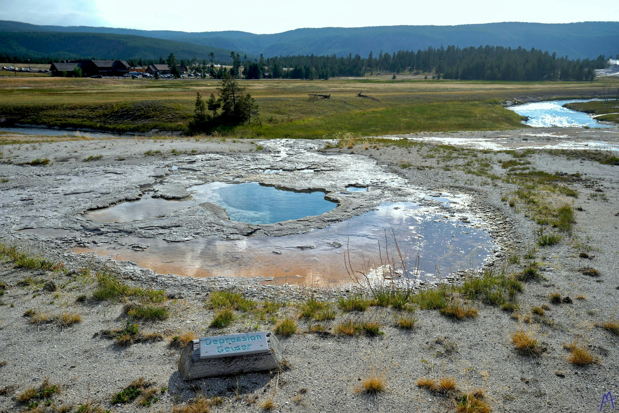 Orange and blue hot spring with river in distance at Yellowstone